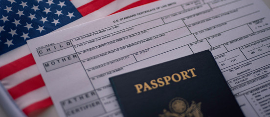U.S. standard certificate of live birth application form next to American flag and Passport of USA. Wide photo. Birthright citizenship concept.