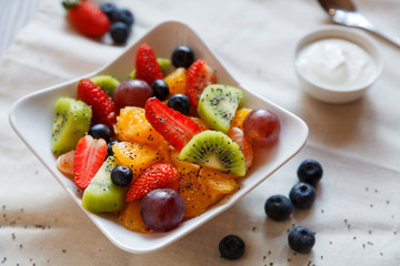 Healthy salad of fresh fruits and chia seeds in a white plate with yogurt on the table.