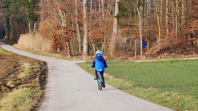 Kleiner Junge f&auml;hrt mit Helm Fahrrad auf einer Landstrasse