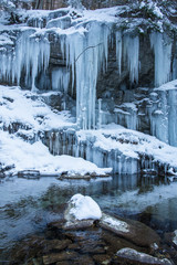 Winter frozen waterfall. Small pond and snowy boulders bellow cascade of waterfall. Crystal freeze water of mountain river and sounds of falling water.