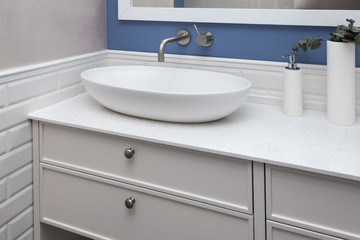 Fototapeta na wymiar Bathroom interior in a blue pastel colors and a close up of a bathroom furniture. A bowl-shaped sink on a ultra thin quartzite countertop. Contemporary bathroom design. 