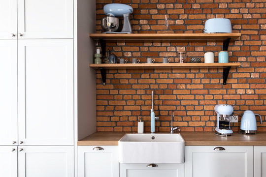 Kitchen in a contemporary shaker style with pastel blue kitchen appliances and orange cooker and the hood. Brick wall backsplash and retro style accessories. Shaker style kitchen. 
