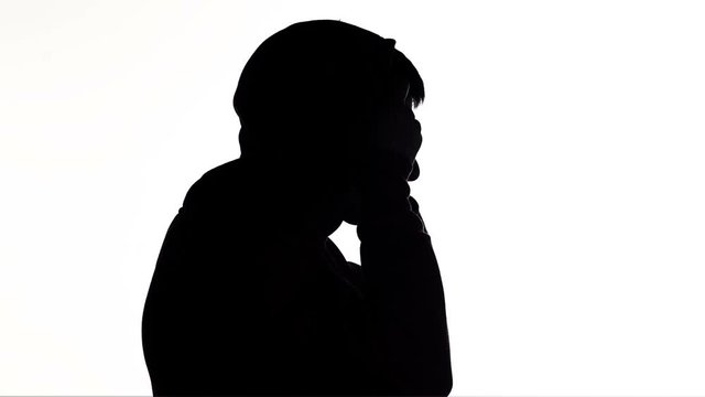silhouette of a young man puts on a hood of a sweatshirt and goes on white isolated background, unknown person, guy hides face, concept fashion