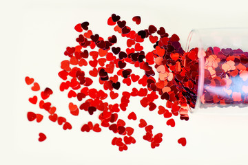 The glass lies on a light background. Red hearts poured out of it. The concept for Valentine's Day