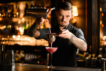 Male bartender pours alcohol cocktail from steel shaker
