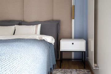 White bed side table with a black metal frame and black handle in a contemporary bedroom interior in pastel blue, sand and bright colors. Modern bedroom look. 