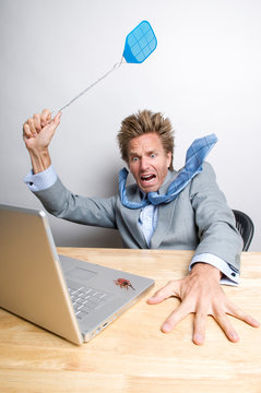 Frightened businessman swatting a bug crawling on his laptop computer