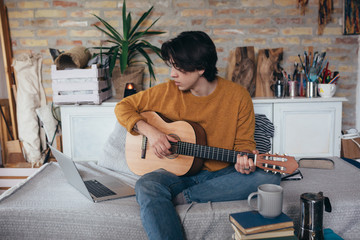 young man playing guitar in his home - obrazy, fototapety, plakaty