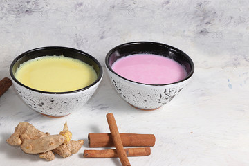Turmeric latte and pink golden milk for a better sleep, ginger and cinnamon on a gray table, a fashionable relaxing drink, has antioxidant properties, helps detoxify the body, a place for text