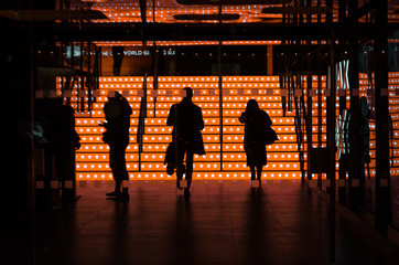 Silhouette of three people coming down some phosphorescent orange stairs inside a dark space