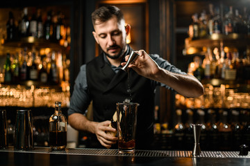 Male bartender pours alcohol from jigger to glass