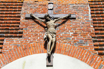 The figure of Jesus Christ crucified on the cross on the wall of an old Christian brick church. Sculpture symbol of Christ on the temple building on Easter day. - obrazy, fototapety, plakaty