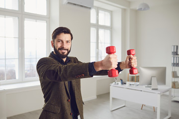 Naklejka na ściany i meble Businessman with a beard is doing exercises with dumbbells in the office during the break.