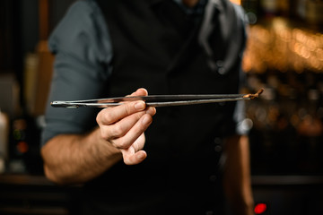 Bartender holding cocktail ingredient with special tongs