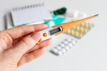 Female hand holding a digital thermometer on white background with pills.
