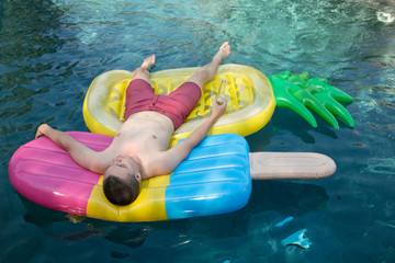 caucasian millennial male floating on pineapple and popsicle raft in outdoor pool getting a tan at a pool party during summer