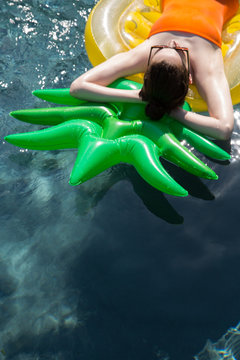 caucasian millennial female floating on pineapple raft in outdoor pool getting a tan at a pool party during summer