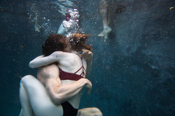 group of millennial friends diving into outdoor pool during summer, couple embracing