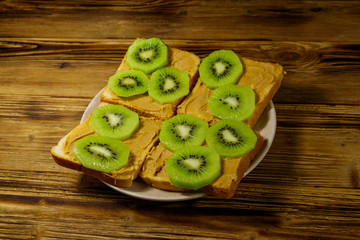 Tasty sandwiches with peanut butter and kiwi fruits on wooden table