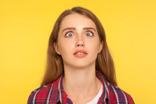 Closeup portrait of funny silly ginger woman in checkered shirt looking up cross eyed with stupid dumb face, girl has awkward confused comical expression. studio shot isolated on yellow background