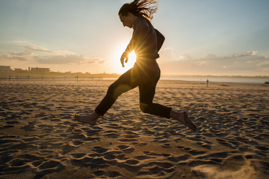 millennial guy running and dancing on beach during sunset