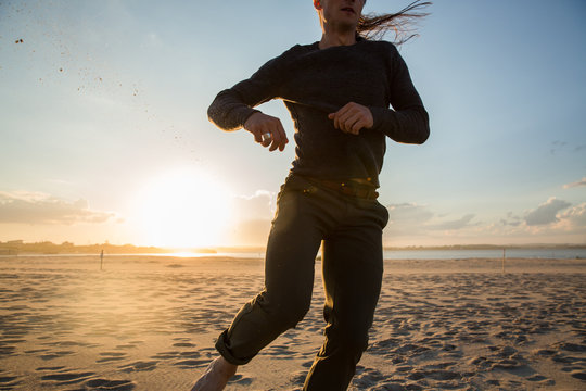 millennial guy running and dancing on beach during sunset