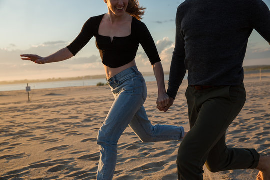 millennial couple on the beach during sunset, guy and girl running