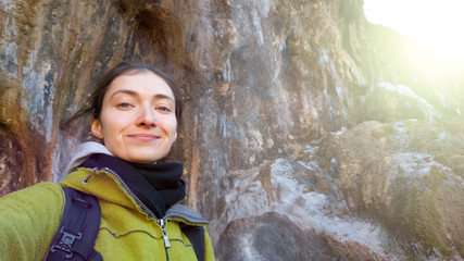 Obraz na płótnie Canvas The girl takes a selfie and smiles against the background of beautiful rocks. Winter trip to nature. Warm coat and backpack
