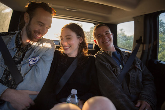 Three young adults sitting in the backseat of a car on roadtrip in summertime, laughing, hip, millennials, androgynous, gender neutral, ethnically ambiguous