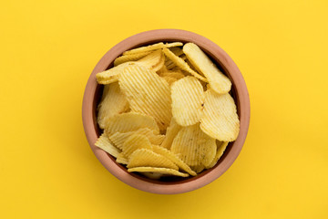 Crispy potato chips in bowl on yellow background, top view, with space for text