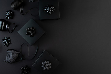 Minimalist black flat lay. Black gift boxes with ribbons on black surface, black friday concept, gift for man, father, husband.
