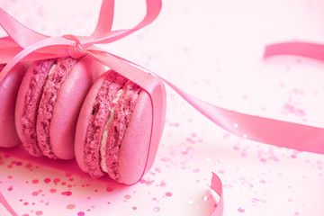 Pink macaroons wrapped in ribbon on glitter background. Pastry party. Pastel color. Romantic background in pink color. Valentine's day mobile wallpaper. Love background for stories. Wedding invitation