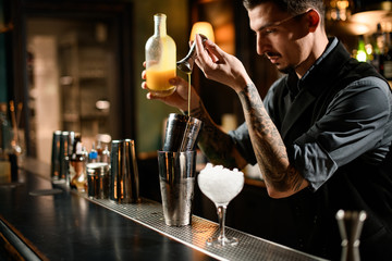 Male bartender prepares alcohol drink with jigger and shaker