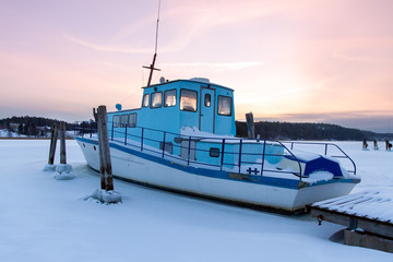 Boat is stuck in ice in the winter, Kaarina, Finland. Beautiful sunset in the background.