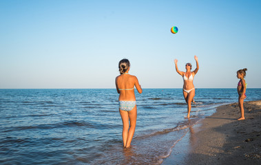 Pretty young woman plays ball with her charming daughters while swimming in the sea on a sunny warm summer day. Vacation concept with children. Advertising space