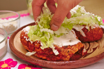 A person is decorating a traditional mexican pambazo with cream, lettuce and white cheese