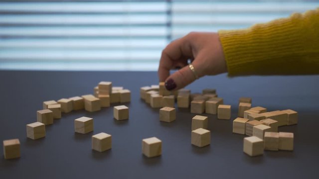 Young female hand with a red manicure in sweater searching for a green coloured wooden block between other mono coloured blocks and put it in the middle of footage. CloseUp video where girl playing wi