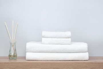 On a shelf in the bathroom are white towels of different sizes neatly folded and next to it is a glass jar with scented balls and wooden sticks. The concept of spa, order in the home, textiles