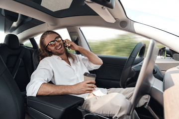 Young adult man sitting in car, talking on smartphone