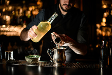 Male bartender pours alcohol from jigger to mug