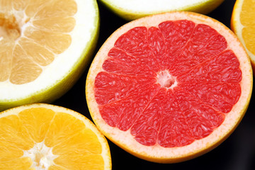 cut pieces of different citrus fruits on dark background