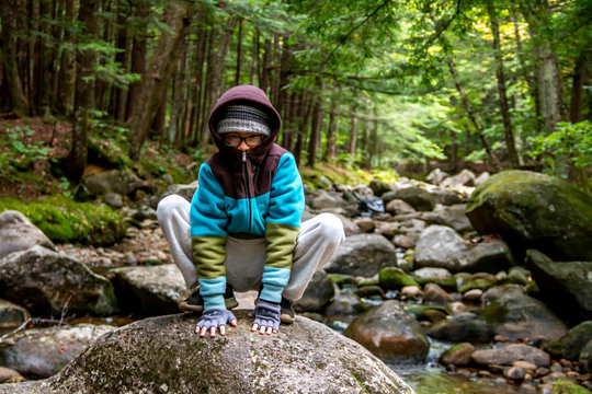 Boy Playing Leap Frog On A Rock In The Woods