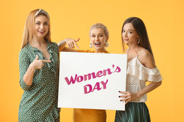Beautiful young girls holding poster with text WOMEN'S DAY on color background