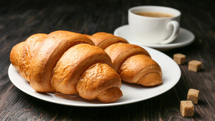 Plate with tasty croissants and cup of coffee on table