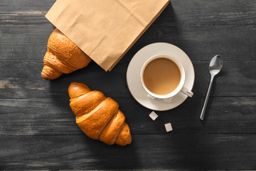 Paper bag with tasty croissants and cup of coffee on wooden table