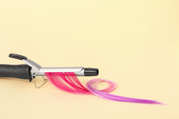 Curling iron and hair strand on color background