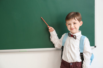 Little schoolboy near blackboard in classroom