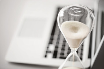 Hourglass with laptop on table in office, closeup. Time management concept