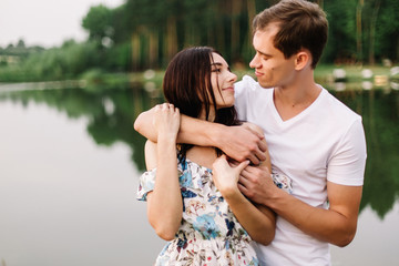 Young loving couple hugging near lake on sunset.