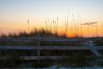 Fototapeta na wymiar Fence and grassy beach as the sun sets